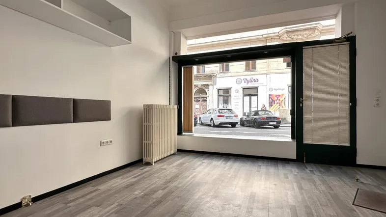 Heller Geschäftsraum mit großem Schaufenster zur Straße, Heizkörper und modernem Laminatboden.