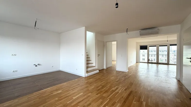 Helles Wohnzimmer mit Parkettboden, Treppenzugang und Blick auf die Stadt.