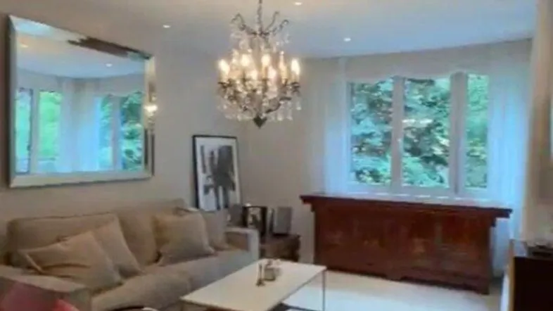 Helles Wohnzimmer mit glänzendem Boden, elegantem Kronleuchter und großem Wandspiegel.