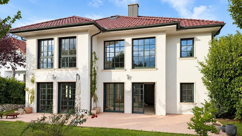 Moderne Villa mit weißer Fassade, roten Dachziegeln und großen Fenstern zum Garten.