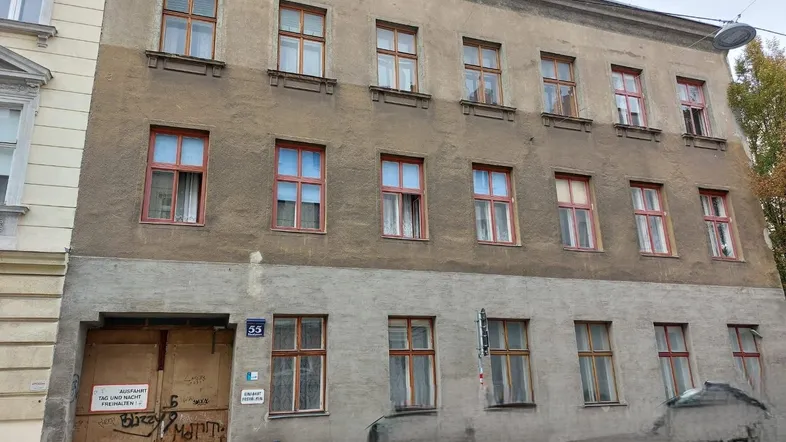 Altes Mehrfamilienhaus mit mehreren Stockwerken und vielen Fenstern, das eine Renovierung benötigt.