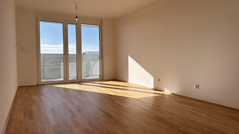 Großes, helles Wohnzimmer mit Parkettboden und Zugang zu einem sonnigen Balkon.