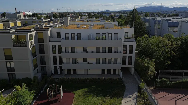 Luftaufnahme einer modernen Wohnanlage mit begrünten Dächern, Spielplatz und Tennisplatz.