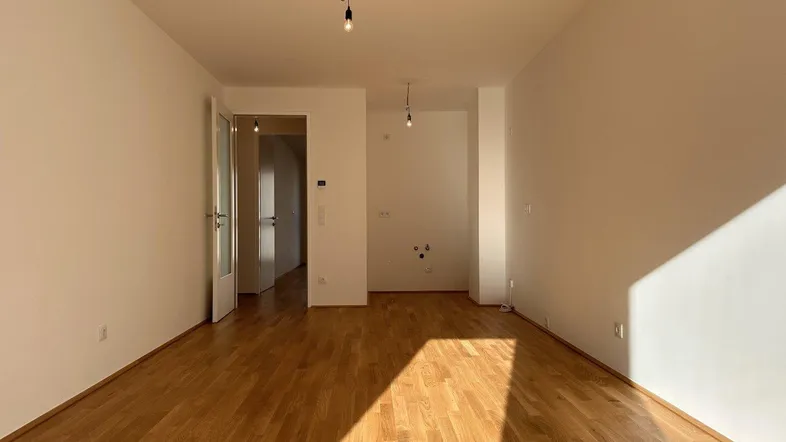 Helles, leeres Zimmer mit Parkettboden und weiß gestrichenen Wänden, bereit zur individuellen Gestaltung.