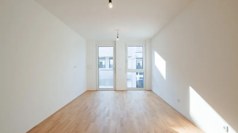 Helles, leeres Zimmer mit Parkettboden und Zugang zu einem Balkon, ideal für Wohn- oder Schlafbereich.