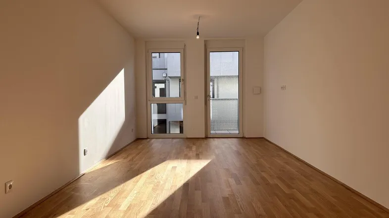 Helles Zimmer mit Parkettboden und Zugang zu einem Außenbereich, durchflutet von natürlichem Sonnenlicht.