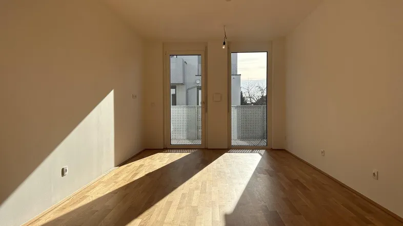 Helles, leeres Zimmer mit Parkettboden und Zugang zu einem französischen Balkon.