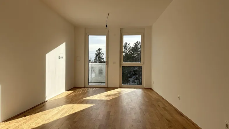 Helles, leeres Zimmer mit Holzboden und Zugang zu einem französischen Balkon.