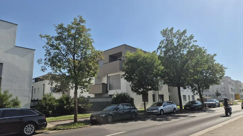 Straßenansicht des modernen Wohnkomplexes mit parkenden Autos und Bäumen entlang der Straße.