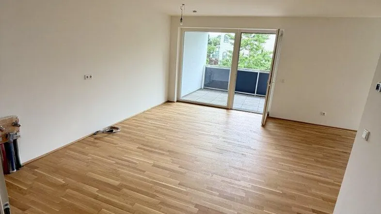 Helles, leeres Zimmer mit Parkettboden und Zugang zu einem Balkon, ideal für Wohn- oder Essbereich.