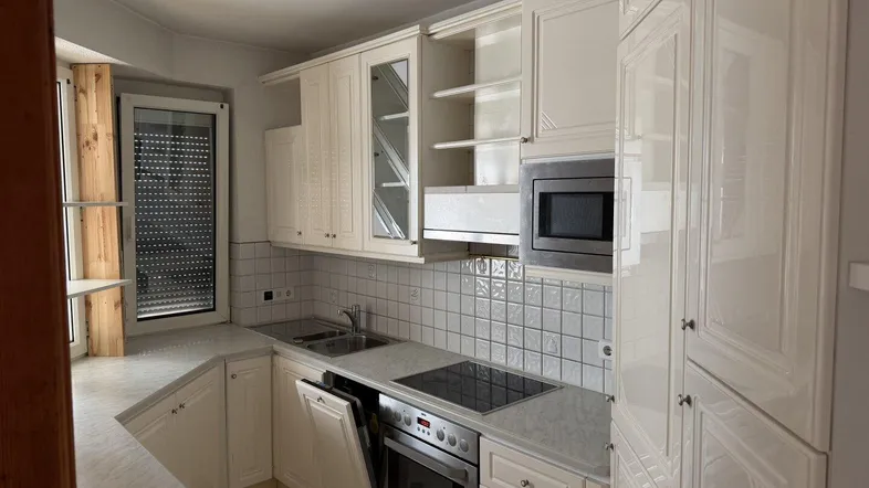 Helle Einbauküche mit weißen Schränken, integrierten Geräten und Fenster mit Rollladen.