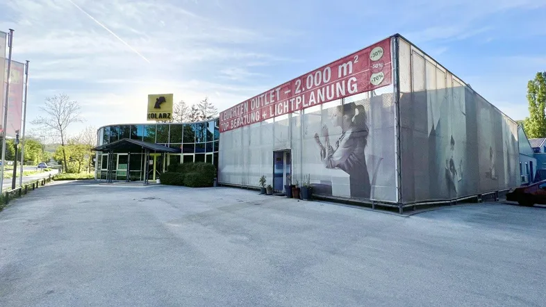 Außenansicht eines Gewerbegebäudes mit großem Werbebanner und weitläufigem Parkplatzbereich.