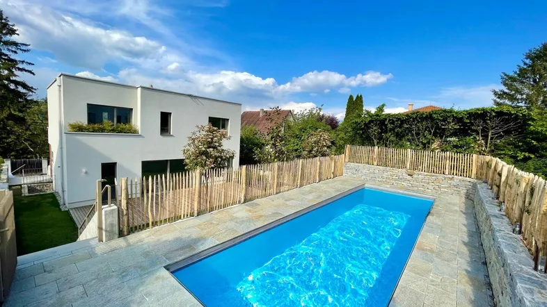 Modernes Haus mit privatem Pool und gepflegtem Gartenbereich unter blauem Himmel.