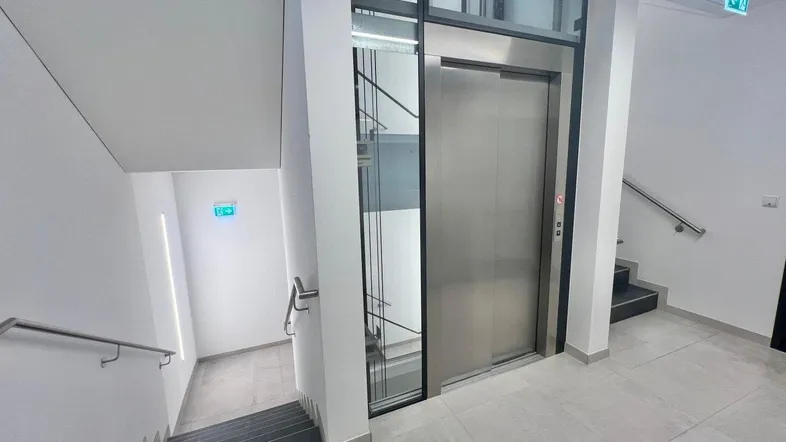 Moderner Eingangsbereich mit Aufzug und Treppenhaus, ausgestattet mit Fliesenboden und Handläufen.