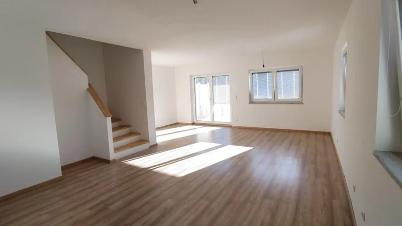Heller, leerer Wohnbereich mit Laminatboden, weiß gestrichenen Wänden und Zugang zur Terrasse.