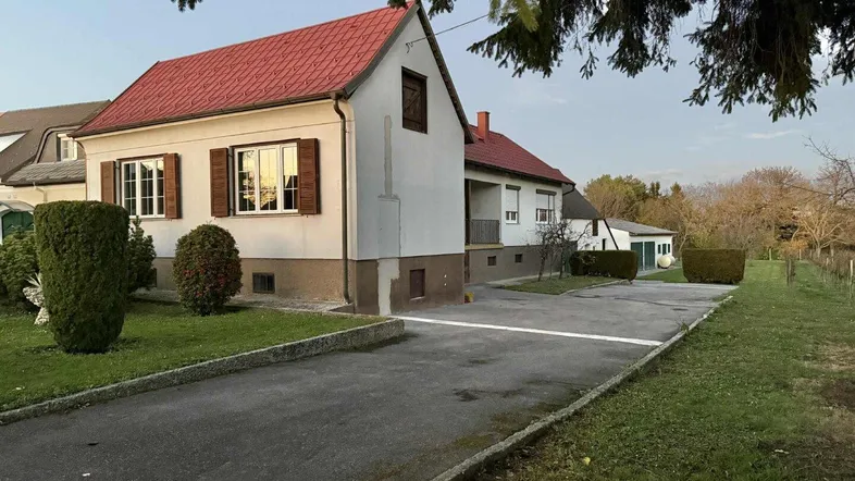 Einfamilienhaus mit rotem Ziegeldach, gepflegtem Vorgarten und Zufahrt bei Tageslicht.