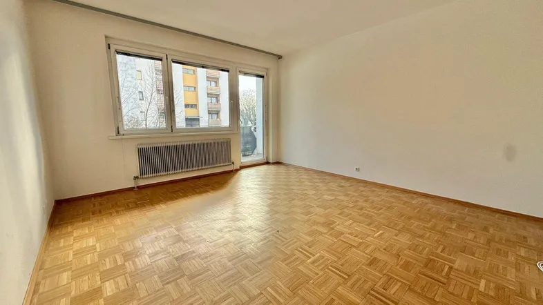 Helles Wohnzimmer mit Fischgrätparkettboden, weißen Wänden und Zugang zum Balkon.