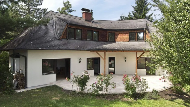 Ansicht des Hauses mit geschwungenem Dach, großer Terrasse und gepflegtem Gartenbereich.