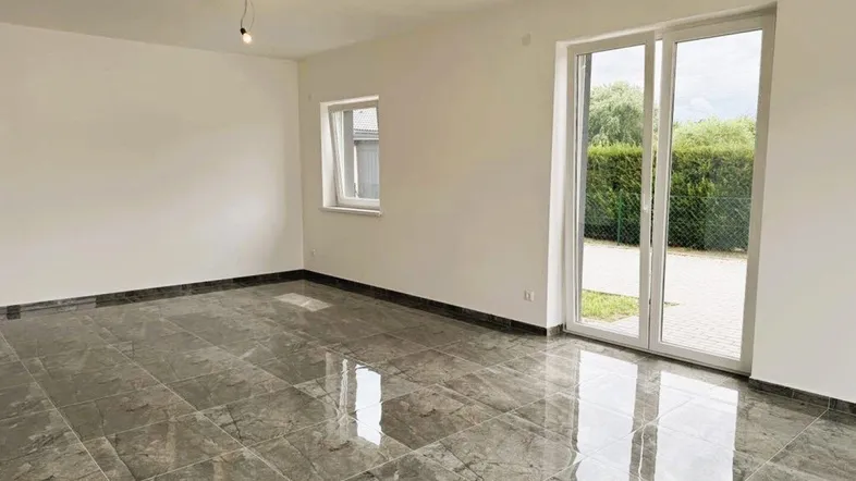 Helles Wohnzimmer mit glänzenden Fliesen und Zugang zum Gartenbereich.