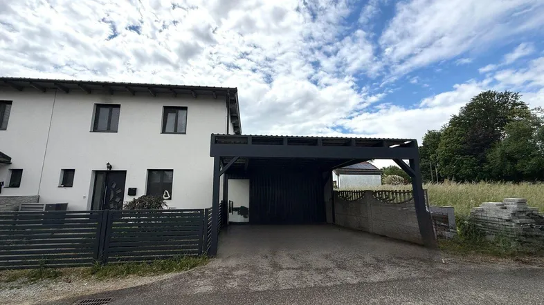 Modernes Reihenhaus mit Carport und Zufahrt unter bewölktem Himmel.