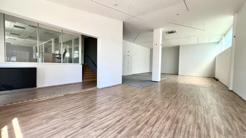 Geräumiger Büroraum mit Holzoptik-Laminatboden, weißen Wänden und großen Fenstern, die viel Tageslicht hereinlassen.