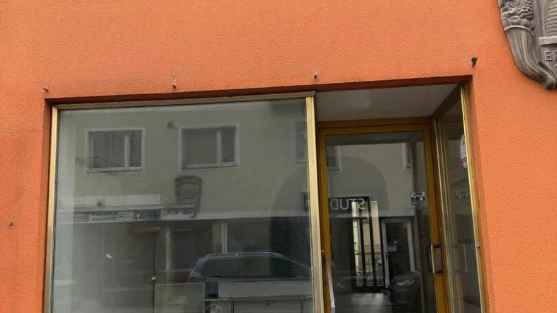 Vorderansicht eines Geschäftsgebäudes mit großer Schaufensterfront und Eingangstür in leuchtendem Orange.