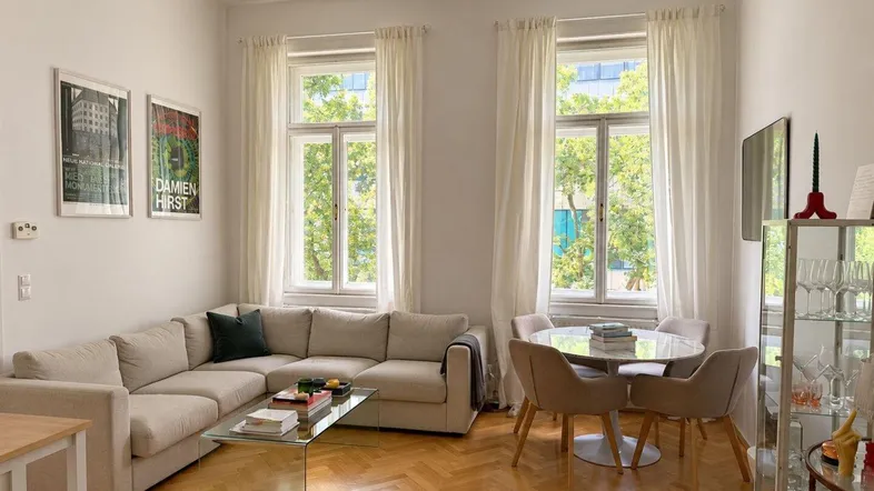 Helles Wohn- und Esszimmer mit beigem Ecksofa, modernem Esstisch und Fischgrätparkettboden.