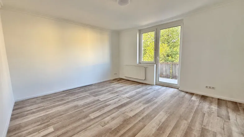 Helles, leeres Zimmer mit Laminatboden und Zugang zu einem Balkon, ideal als Wohn- oder Schlafzimmer.