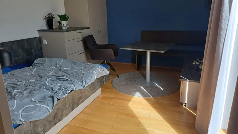 Helles Schlafzimmer mit Holzboden, blauer Akzentwand und kleinem Essbereich.