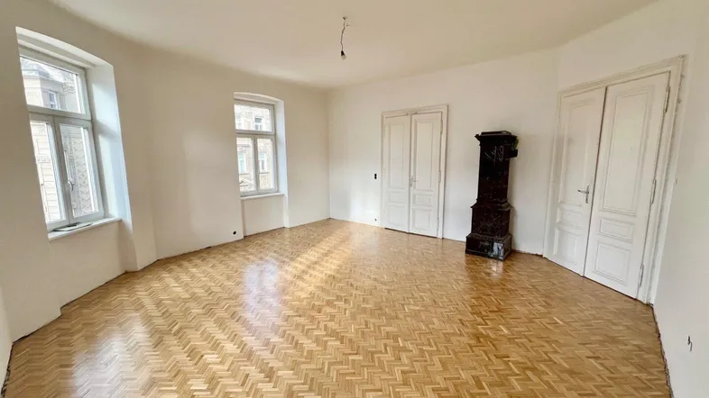 Helles Wohnzimmer mit Fischgrätparkett, hohen Türen und einem traditionellen Kachelofen.