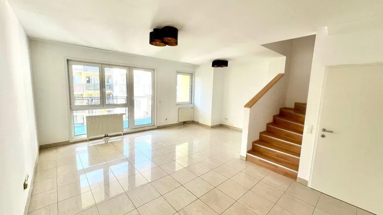 Heller Wohnbereich mit Fliesenboden, großzügigen Fenstern und Zugang zu einem Balkon.