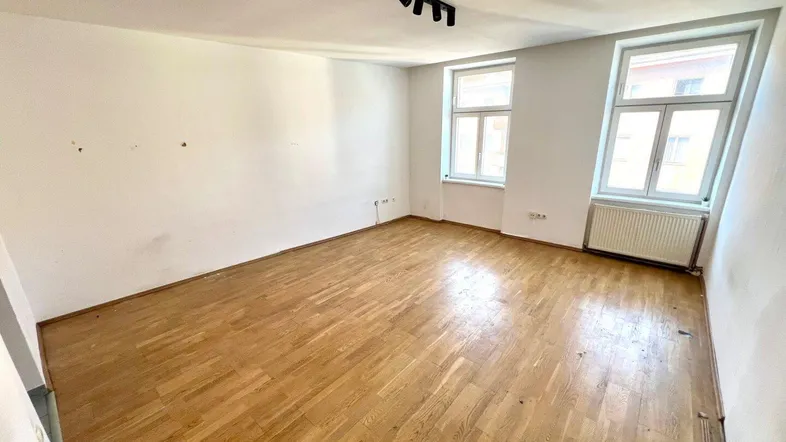 Helles, leeres Zimmer mit Holzparkettboden und zwei Fenstern, bereit zur individuellen Gestaltung.