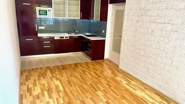Moderne Einbauküche in Dunkelrot mit integrierten Geräten und hellem Parkettboden, angrenzend an einen Wohnbereich.