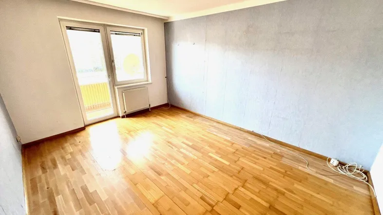 Helles Zimmer mit Parkettboden und Zugang zu einem Balkon, ideal als Wohn- oder Schlafzimmer.