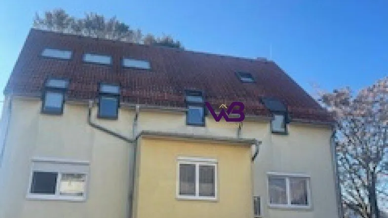 Mehrstöckiges Gebäude mit gelber Fassade, rotem Ziegeldach und vielen Dachfenstern.
