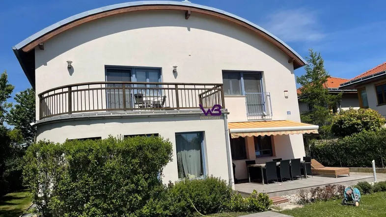 Modernes Haus mit geschwungener Fassade, Balkon, Terrasse und Pool im Garten.