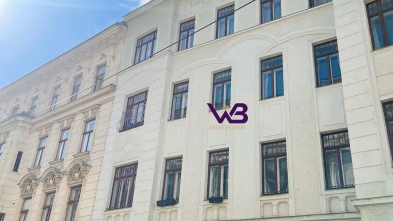 Klassisches Mehrfamilienhaus mit weißer Fassade und traditionellen Fenstern unter blauem Himmel.