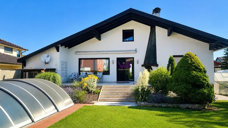 Rückseite des Hauses mit gepflegtem Garten, Rasenfläche und überdachtem Poolbereich unter blauem Himmel.