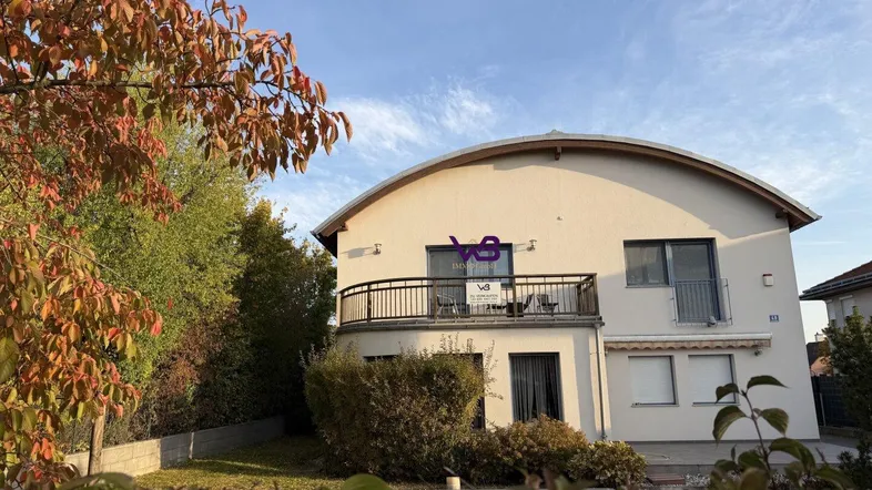 Modernes Haus mit geschwungener Dachlinie, Balkon und gepflegtem Vorgarten im Herbstlicht.