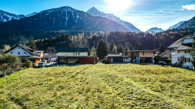 Weitläufiges Grundstück mit Blick auf die umliegenden Berge und mehrere Wohnhäuser unter strahlender Sonne.