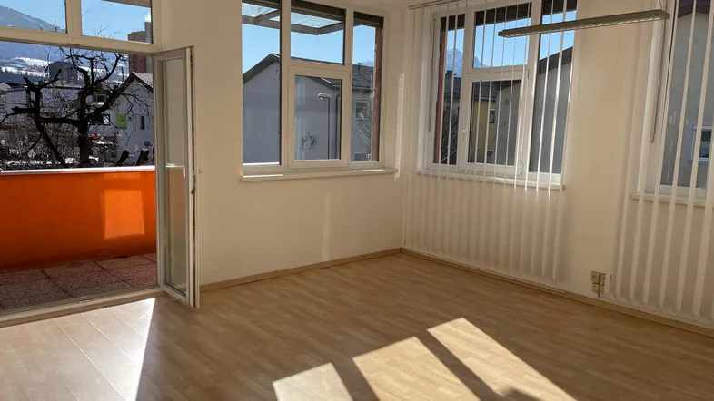 Helles Zimmer mit Laminatboden, großen Fenstern und Zugang zu einem sonnigen Balkon mit Bergblick.