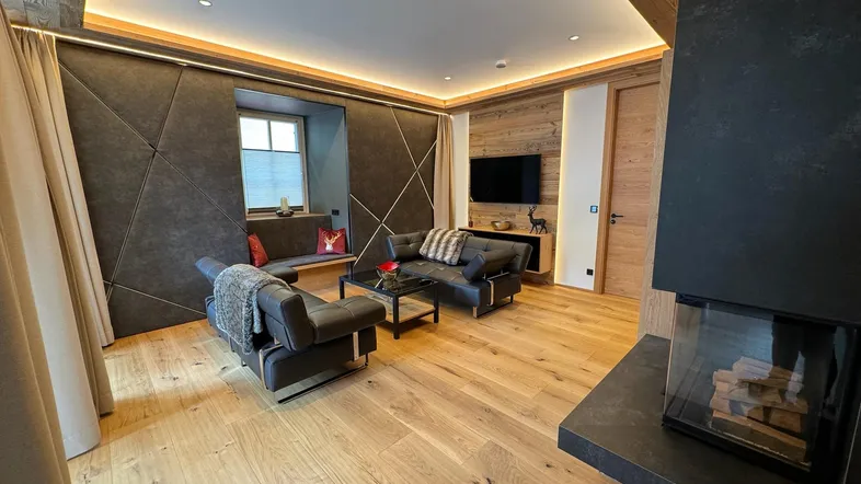 Modernes Wohnzimmer im alpinen Stil mit Kamin, Holzboden und gemütlicher Sitzecke.