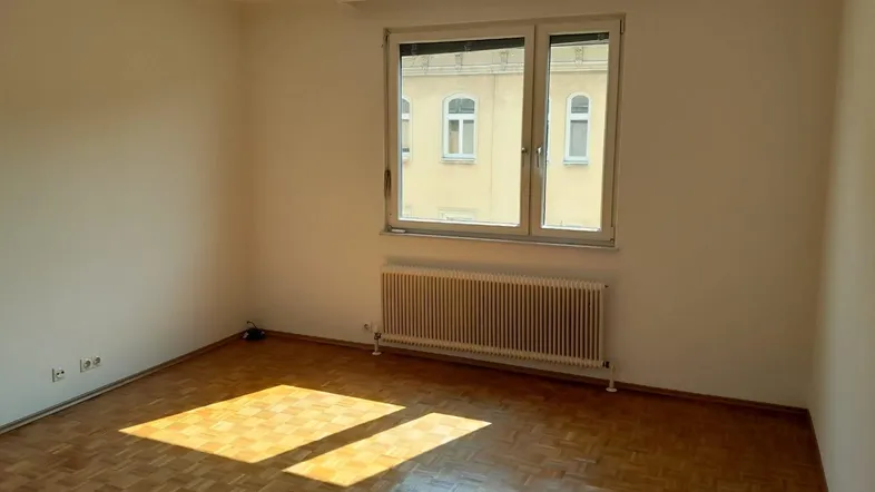 Helles Zimmer mit Parkettboden und großem Fenster, das viel Sonnenlicht hereinlässt.