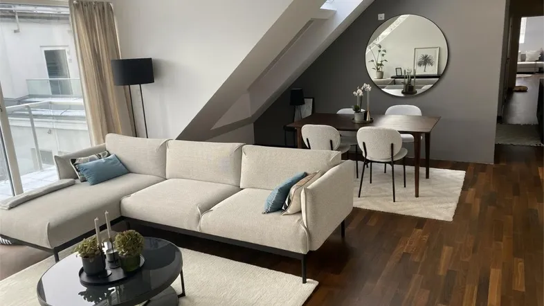 Heller Wohn- und Essbereich mit Dachschrägen, dunklem Parkettboden und modernem Sofa.