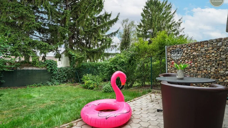 Gepflegter Garten mit Rasenfläche, gepflasterter Terrasse und Gabionenwand.