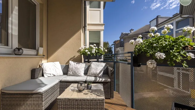 Sonniger Balkon mit bequemen Rattanmöbeln und blühenden Pflanzen, ideal zum Entspannen.