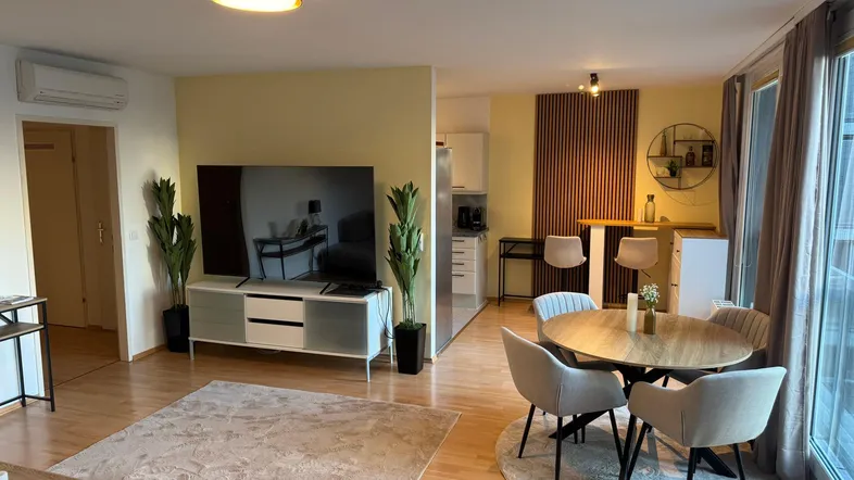 Helles Wohn- und Esszimmer mit Holzboden, moderner Einrichtung und Zugang zum Balkon.
