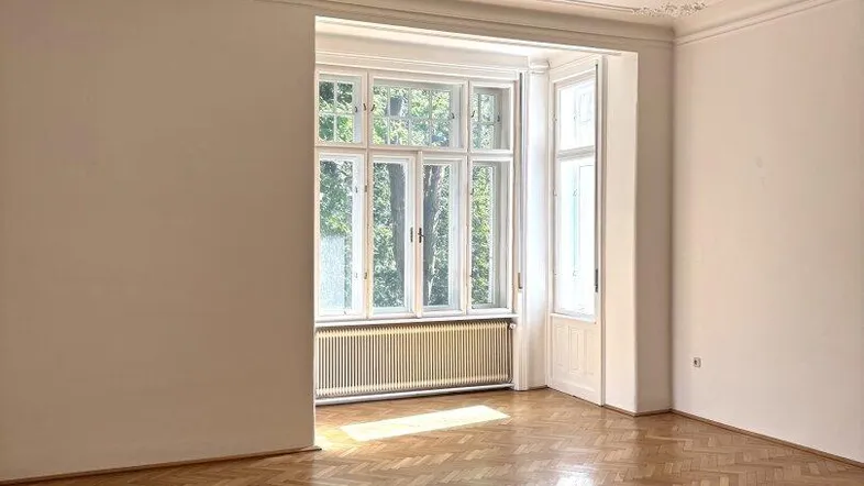 Helles Wohnzimmer mit Fischgrätparkett, Stuckdecke und großen Fenstern.