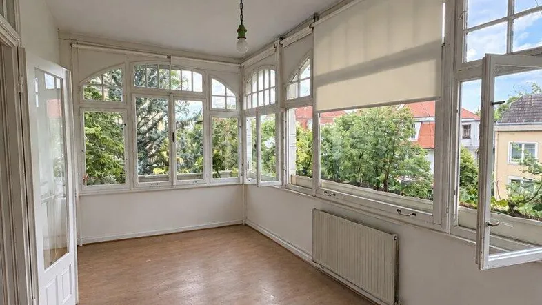 Heller Raum mit vielen Fenstern, Holzboden und Blick ins Grüne, ideal als Wintergarten oder Veranda.