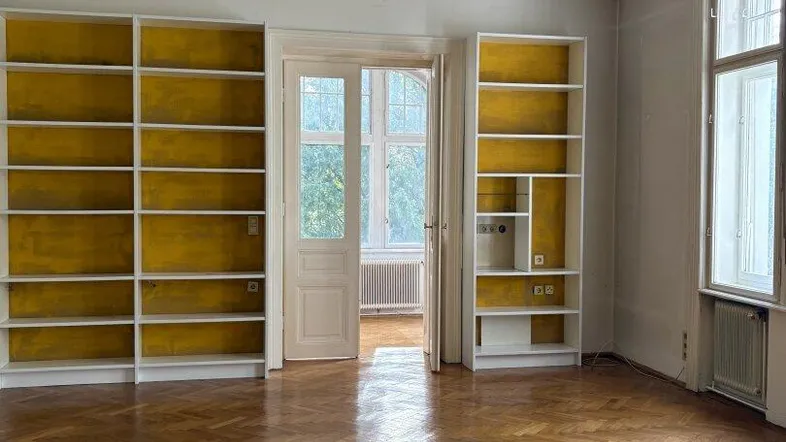 Wohnzimmer mit integrierten gelben Regalen, Fischgrätparkett und Zugang zu einem weiteren Raum.